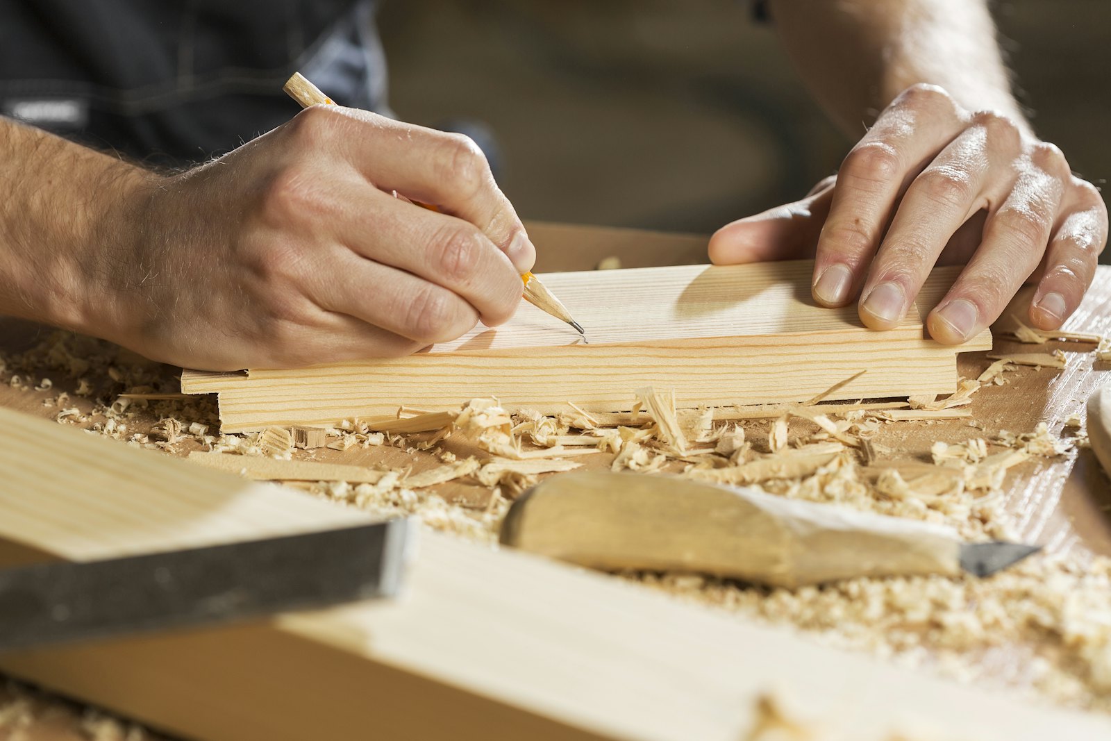 A joiner marking a cutting line on a timber board with a pencil