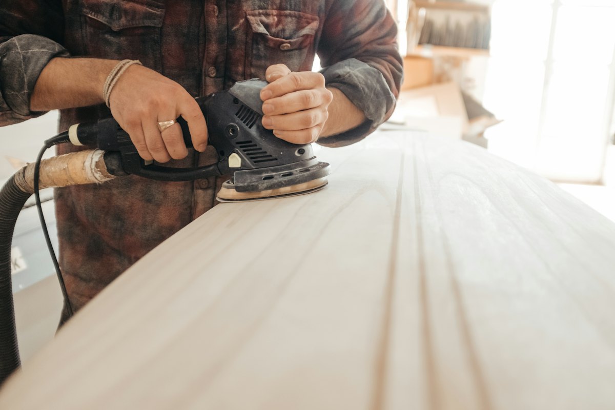 A joiner sanding a pale timber tabletop